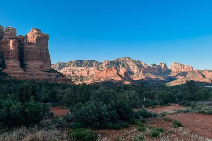 a sedona desert landscape with orange rock mountains in the distance with the sunlight illumiating the mountains