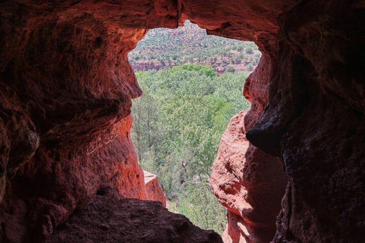 an opening of a Sedona cave with a view of trees and red rocks.