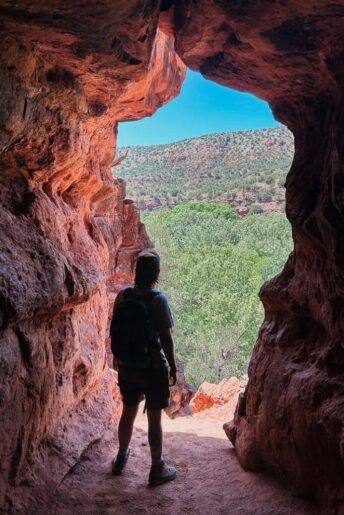 Standing at an opening of a cave looking out at the view of red rock mountains