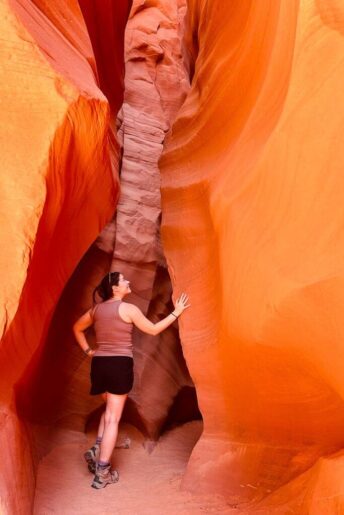 Jess standing at the entrance of Antelope Canyon X with her hand on the wavy orange wall 