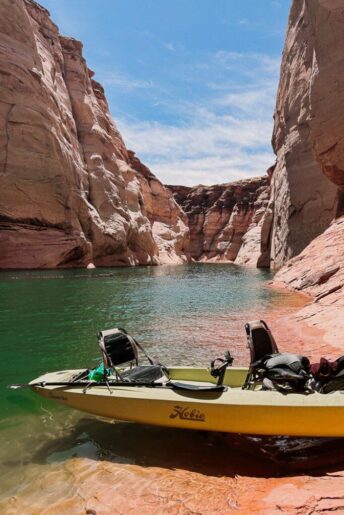 A green kayak pulled up on a rock face with towering canyon walls and bright green water behind it